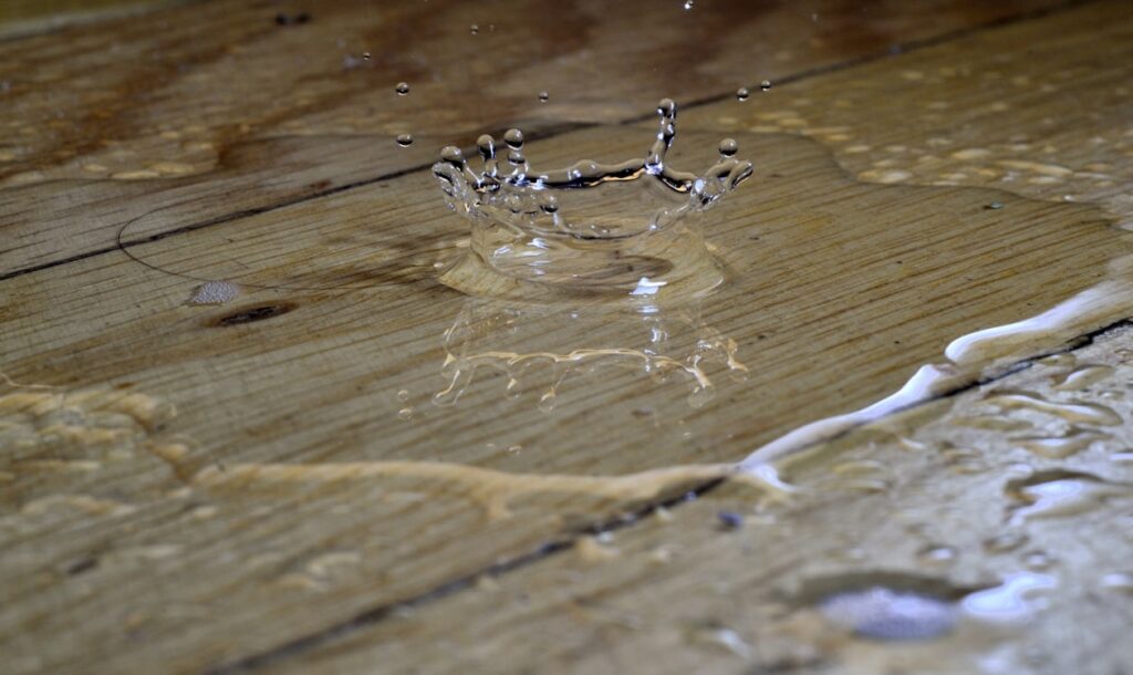 Water splashing onto a hardwood floor, showing moisture that can cause warping, staining, and water damage without fast cleanup.