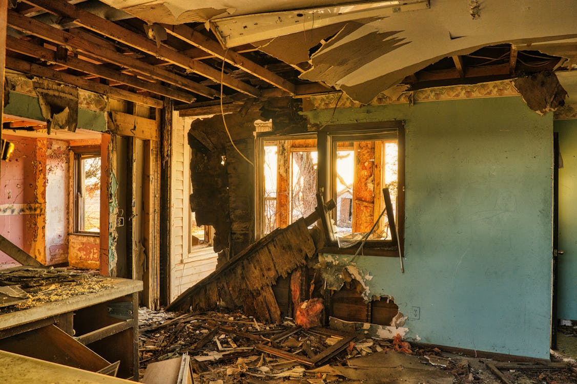 Severely damaged home interior with collapsed ceiling, exposed framing, and debris, showing extensive restoration needs after major property damage.