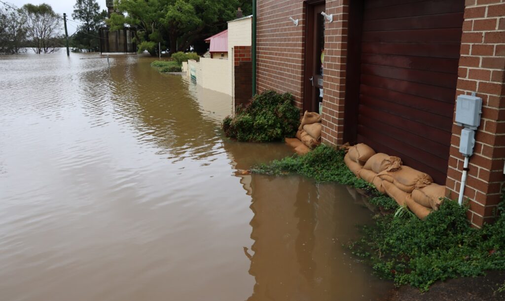 Floodwater surrounding a brick home with sandbags near the doors, showing the need for emergency flood cleanup and water damage restoration.