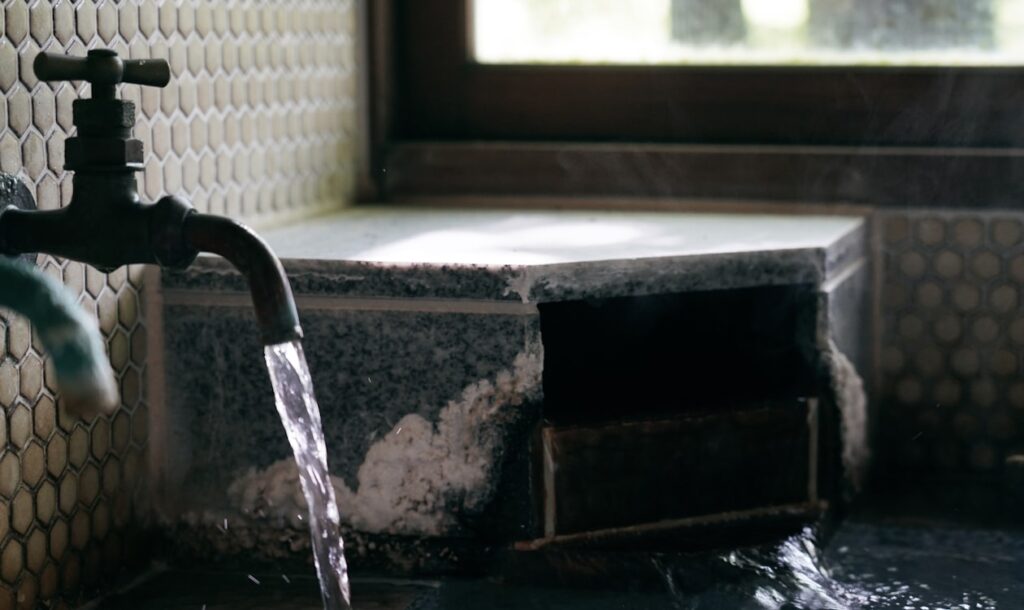 Running faucet spilling water into a damaged tiled area with standing water, highlighting the risk of indoor water damage and mold growth.