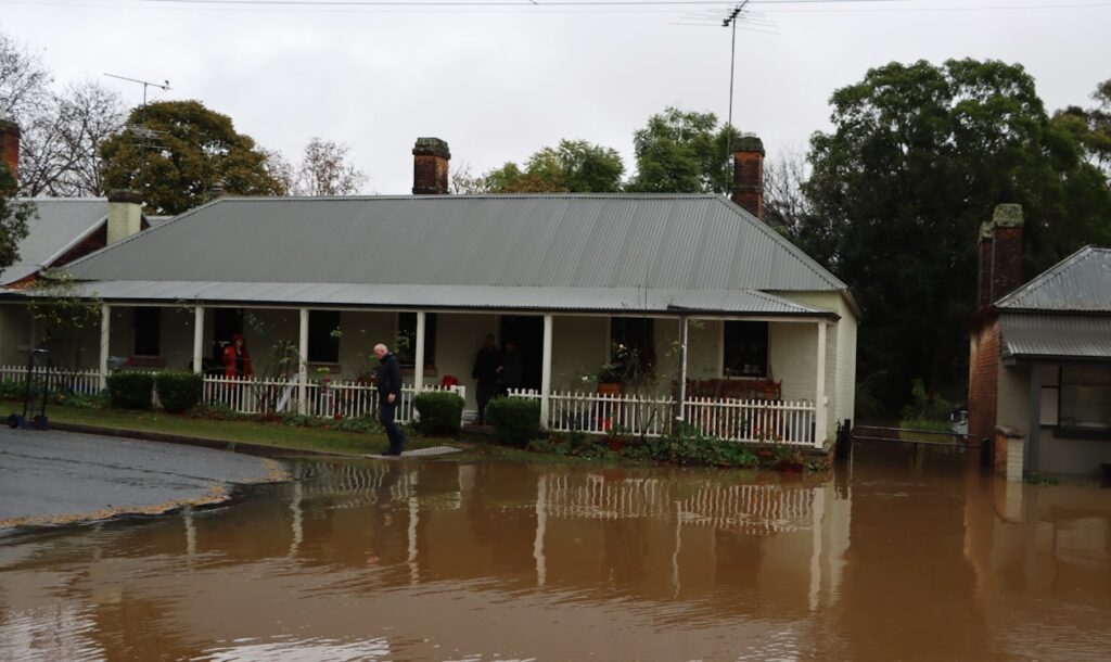 Muddy floodwater surrounding a residential home and street, showing exterior flooding that can lead to water damage cleanup and restoration needs.