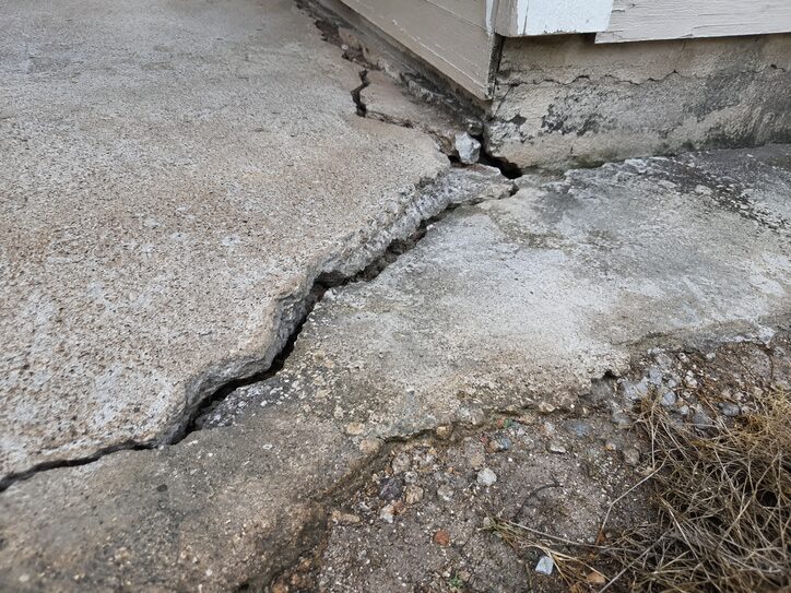 Close-up of cracked concrete near a home foundation showing water damage, erosion, and structural deterioration in North Texas.