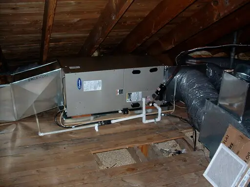 Residential attic air handler with condensate drain line and ductwork during HVAC installation or maintenance.