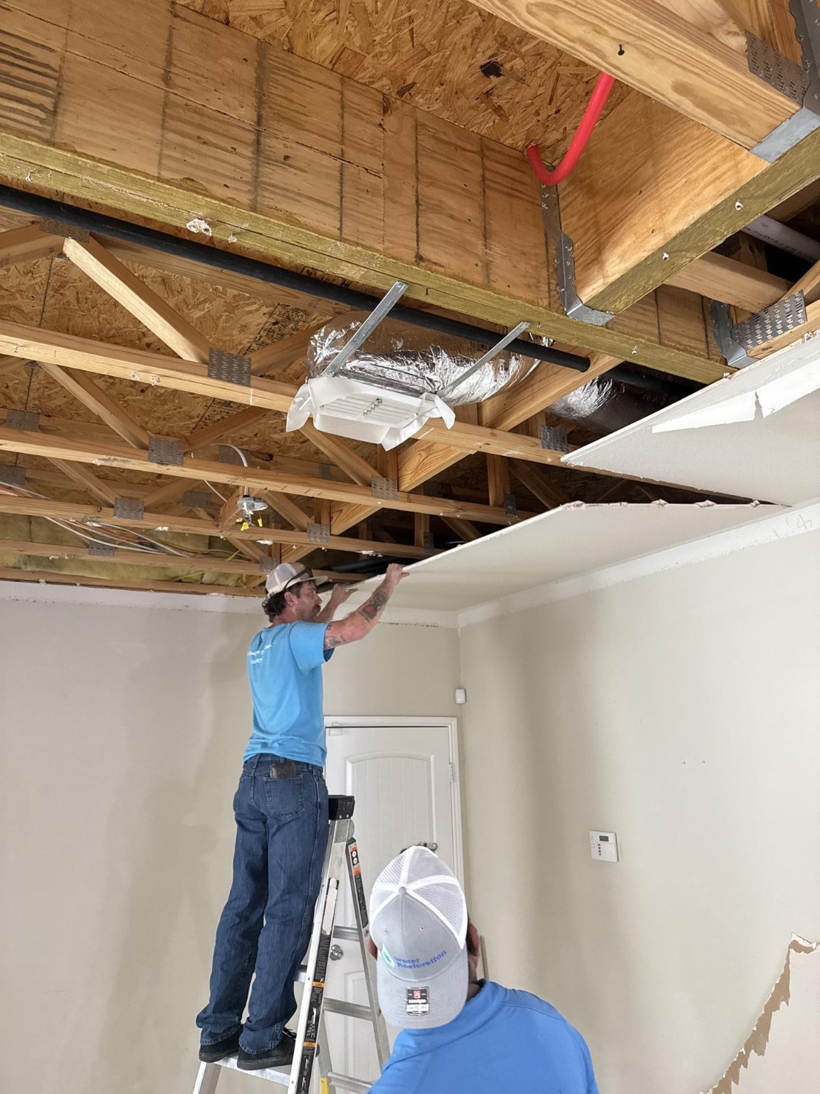 Crew removing ceiling drywall beneath exposed framing
