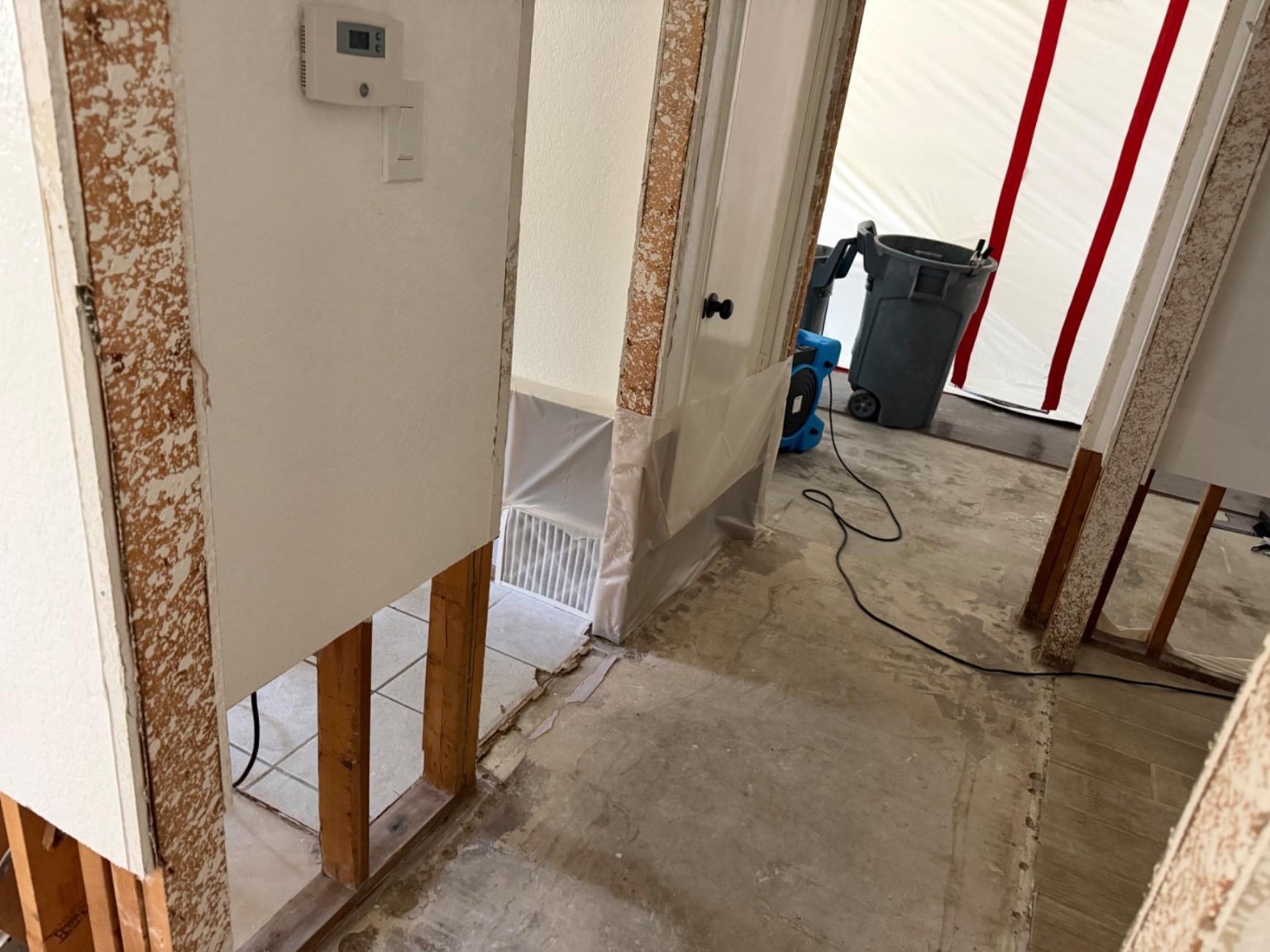 Air mover beside exposed wall framing and a plastic containment barrier